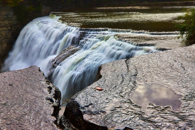 Natte rotsen op de voorgrond door een enorme waterval die over kliffen stroomt