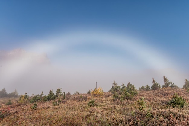 Natural arch fog bow on meadow with blue sky in national park