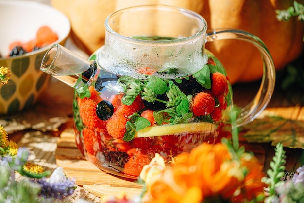 Natural aromatic fruit tea in a transparent teapot and in a cup\
among berries and flowers warming aromatic tea with a deep aroma of\
berries and wildflowers