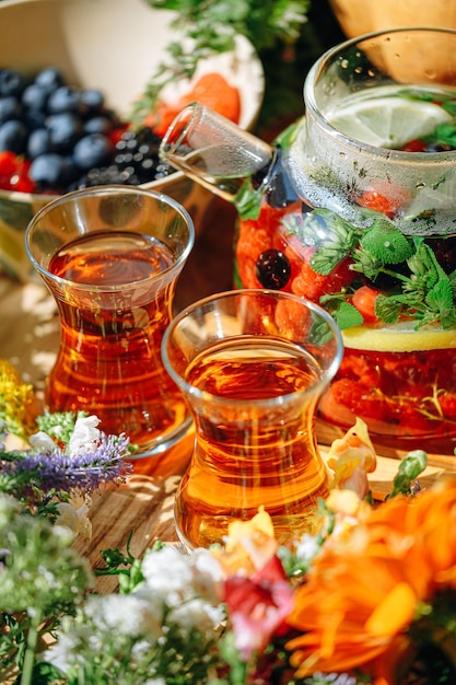 Natural aromatic fruit tea in a transparent teapot and in a cup\
among berries and flowers warming aromatic tea with a deep aroma of\
berries and wildflowers