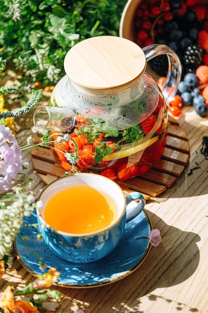 Natural aromatic fruit tea in a transparent teapot and in a cup\
among berries and flowers warming aromatic tea with a deep aroma of\
berries and wildflowers