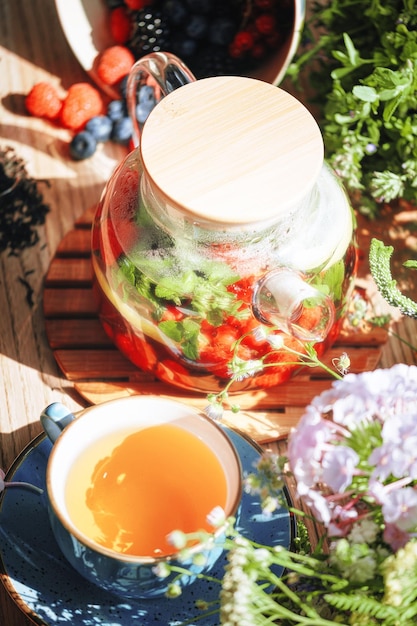 Natural aromatic fruit tea in a transparent teapot and in a cup
among berries and flowers warming aromatic tea with a deep aroma of
berries and wildflowers