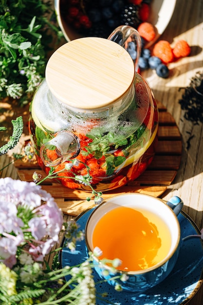 Natural aromatic fruit tea in a transparent teapot and in a cup\
among berries and flowers warming aromatic tea with a deep aroma of\
berries and wildflowers