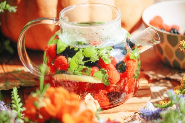 Natural aromatic fruit tea in a transparent teapot and in a cup among berries and flowers warming aromatic tea with a deep aroma of berries and wildflowers