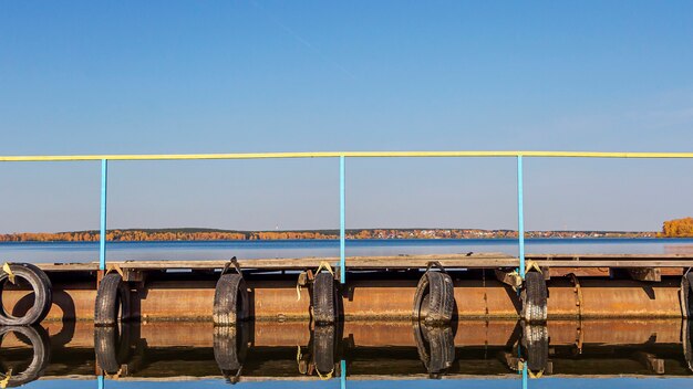 Natural autumn landscape. Old pier on lake with machine tires.