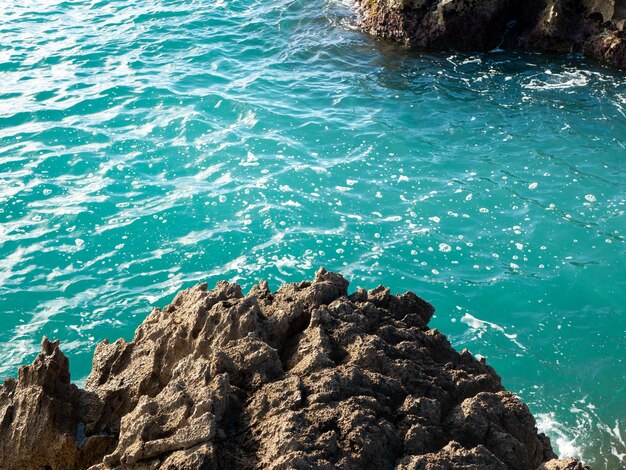 natural background with rough dark rocks surrounded by bright blue slightly wavy sea water surface