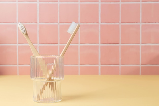 Natural bamboo eco friendly toothbrushes in a glass on table inside a bathroom wall tiles ceramic background Copy space