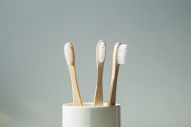 Natural bamboo toothbrushes in a glass on a light background Wooden ecological toothbrushes copy space