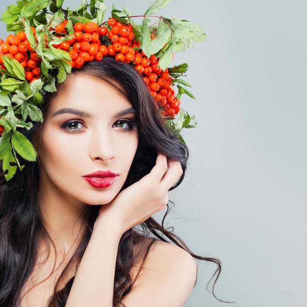 自然の美しさ化粧の長いウェーブのかかった髪と赤いベリーと頭に緑の葉を持つかわいい若い女性