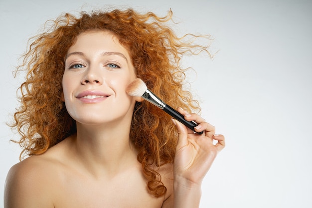 Natural beauty. Delighted red-haired female person expressing positivity while doing face contouring, preparing for meeting