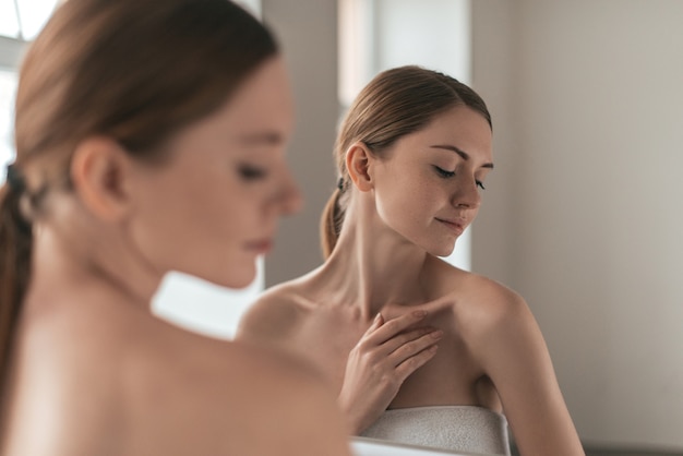 Natural beauty. Over the shoulder view of young woman touching her skin and looking away while standing in front of the mirror