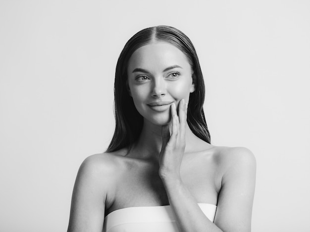 Natural beauty woman with heands touching face long brunette hair beautiful neck and shoulders. Studio shot. Monochrome. Gray. Black and white.