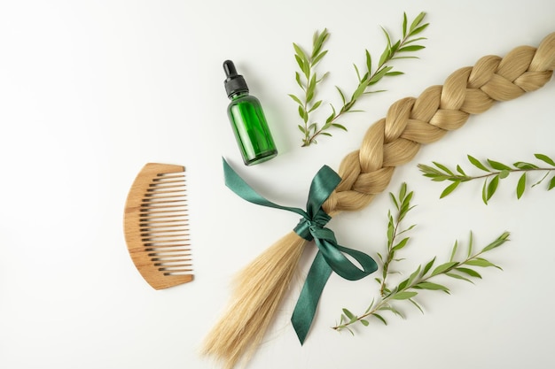 Treccia di capelli biondi naturali e olio essenziale per il trattamento dei capelli in capsule dorate su sfondo bianco