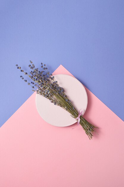 Natural branch of lavender flowers on a round ceramic board on a duotone pastel wall, copy space.  Top view.