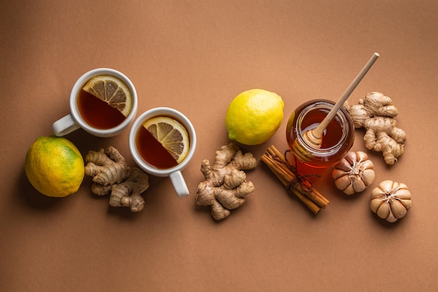 Натуральные домашние средства от простуды и гриппа: чашки горячего чая с лимоном, медом, имбирем и чесноком для укрепления иммунной системы. Натуральные ингредиенты здоровой пищи для стимуляции иммунитета и против вирусов. Вид сверху