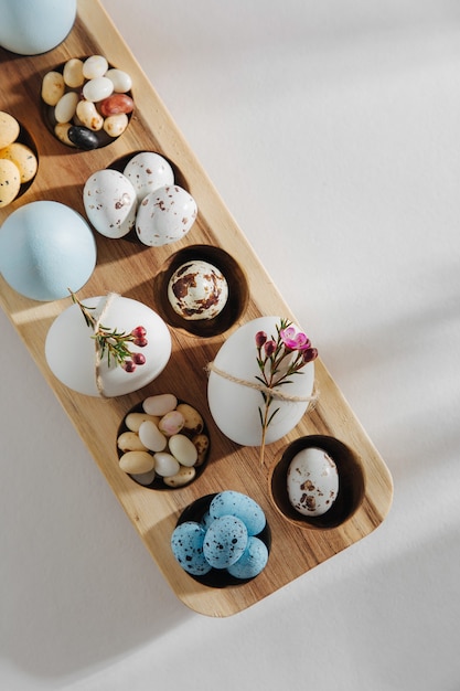 Natural Colored Eggs with flowers, easter chocolate eggs, candy and jelly bean in wooden egg box with sunlights. Stylish Compositions. Flat lay, top view