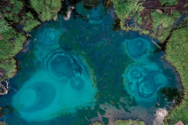 A natural copter view with a landmark on a large azure clear stream in the forest near a grassy bank.