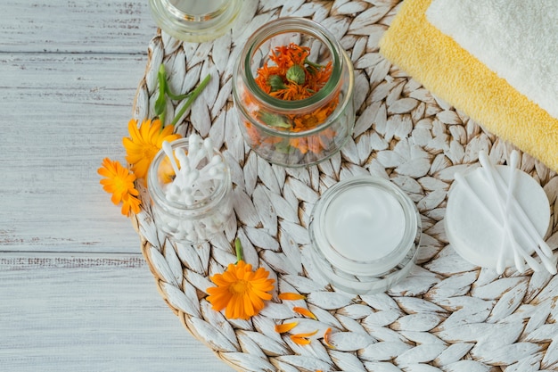 Crema cosmetica naturale, balsamo o unguento, dischetto di cotone, bastoncini e asciugamani con fiori secchi e freschi di calendula.