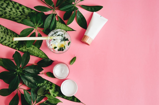 Natural cosmetics and green leaves on pink table.