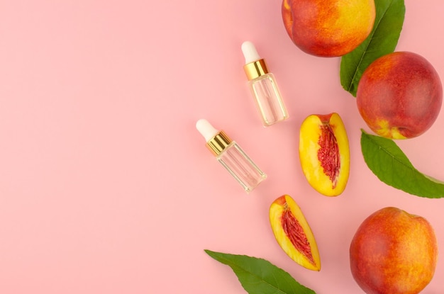 Natural cosmetics hair care Natural peach oil Two bottles with essential peach oil peaches and green peach leaves on a pink background