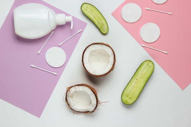 Natural cosmetics, skin care products. Coconut, cucumbers, bottle of cream, cosmetic accessories on colored background. Minimalistic beauty concept.