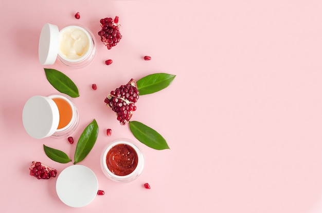 Natural cosmetics with fruit AHA acids, pomegranate extract on pink background. beauty concept. jar with cream, mask, scrub, peeling for professional facial skin care. banner, layout, copy space