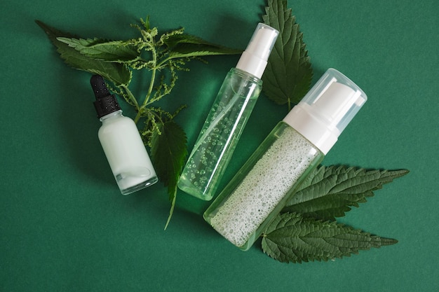 Natural cosmetics with nettle leaves. Lotion, cream, shampoo in mock up bottles, skin care and hair treatment on green background