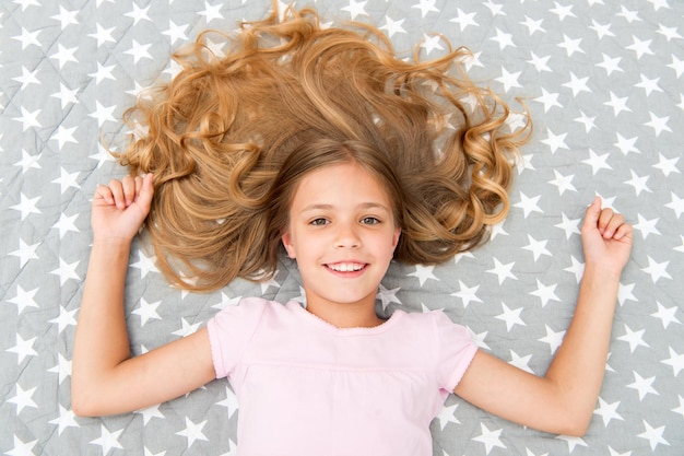 Natural curls treat and care Girl child with long curly hair lay on bed top view Child perfect curly hairstyle looks cute Conditioner mask organic oil keep hair shiny healthy Amazing curls tips