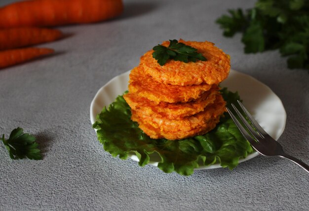 Natural dietary carrot pancakes on a plate with lettuce leaves and a fork on a gray background