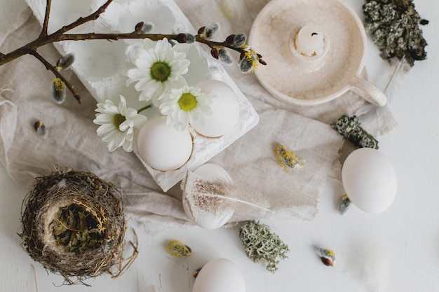 Natural easter eggs feathers willow branches nest and candle on rustic white table flat lay