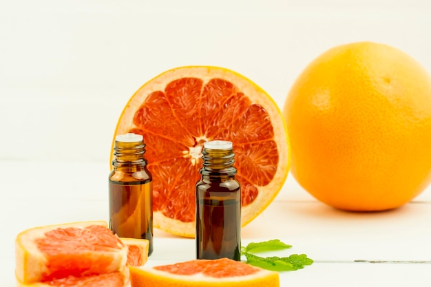 Natural essential oil of grapefruit fruits in glass medical bottles with a dropper against the background of a white brick wall.