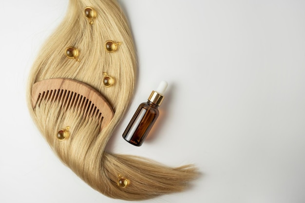 A natural essential oil or serum for hair care in golden\
capsules lying on a strand of blonde hair hair care and smoothing\
concept