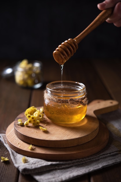 Natural floral honey drains to jar on wood background. Front view