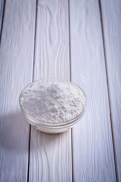 Natural flour in glass bowl on white painted old wooden board food and drink concept