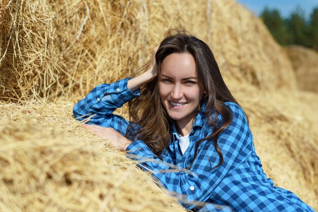 Natural frontal portrait of a smiling young woman standing leaning on a haystack