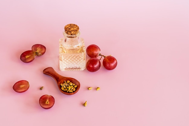 Olio di semi d'uva naturale in una bella bottiglia con coperchio su sfondo rosa tra bacche rosse e semi d'uva cura biologica