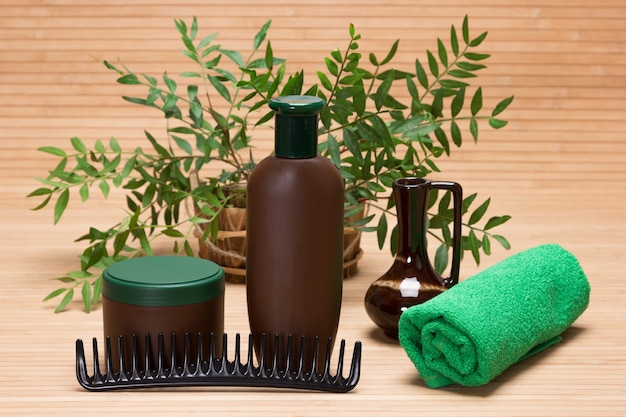 ナチュラルヘアケア化粧品。緑の植物の枝とシャンプー、ヘアマスク、くし、タオル