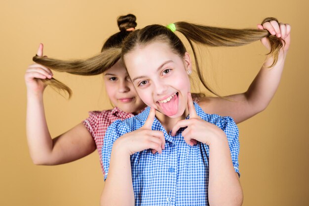 Natural hair extensions Little child keeping long hair of her sister Small girl smiling with blond hair Cute happy kid with fashionable hair ponytails