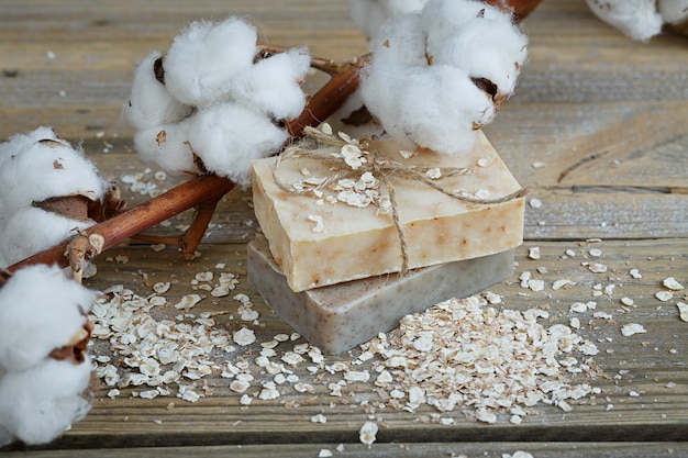 Natural handmade soap, oat flakes and cotton branch on wooden surface