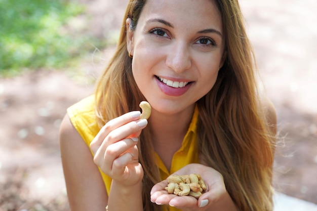 Photo natural healthy girl picking cashew nuts from her hand in the park looks st camera