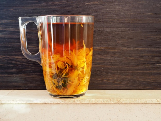 Natural herbal tea made from calendula Glass mug with infusion on a dark background The concept of using medicinal herbs Copy space