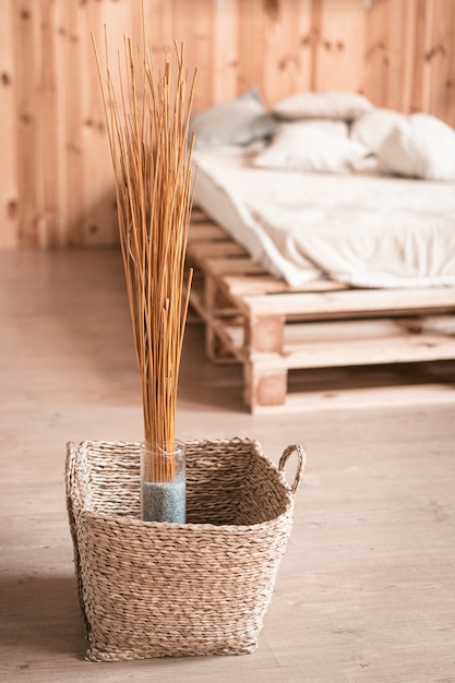 Natural home decor in wooden interior of bedroom. Bouquet of dried sticks in vase and wicker basket at floor.