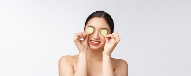 Фото Натуральная домашняя свежая огуречная прокладка для глаз маски для лица азиатская женщина, держащая огуречные прокладки и улыбка расслабиться с натуральной домашней