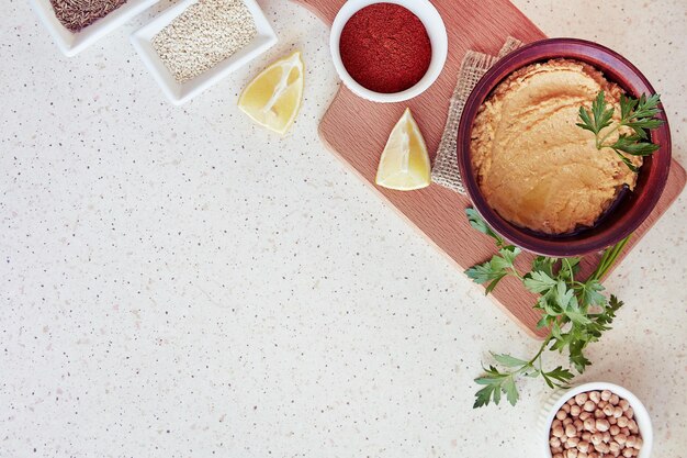 Foto hummus naturale sul tavolo da taglio con prezzemolo, limone, paprika, semi di cumino romano