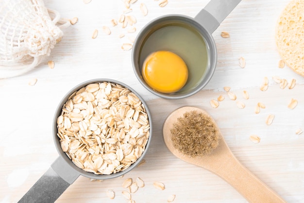 Natural ingredients for a homemade body scrub mask oatmeal and egg in measuring spoons