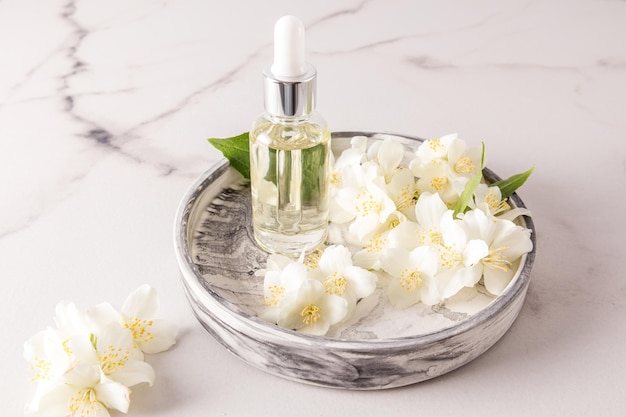 Natural jasmine oil in a glass bottle with a pipette on a round plaster tray with white flowers of the plant organic selfcare