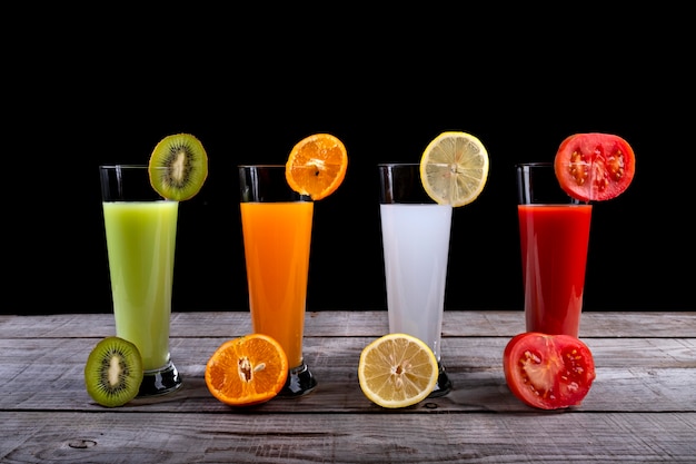 Natural juices of kiwi, orange, lemon and tomato on a black background