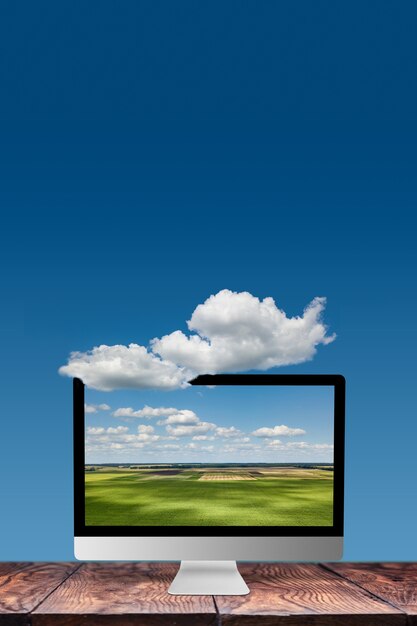 Natural landscape on a computer monitor on a wooden table against blue sky background with white cloud, copy space. working on nature, outside office work concept.