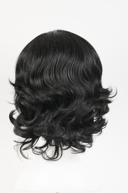 Натурально выглядящий черный парик на белой голове манекена Вьющиеся волнистые волосы средней длины на металлическом держателе для парика, изолированные на белом фоне, вид сзади