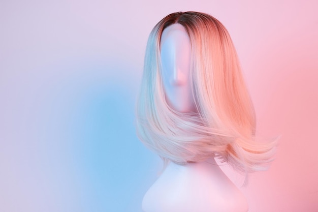 Natural looking blonde fair wig on white mannequin head Middle length hair cut on the plastic wig holder isolated on white background pink lighting